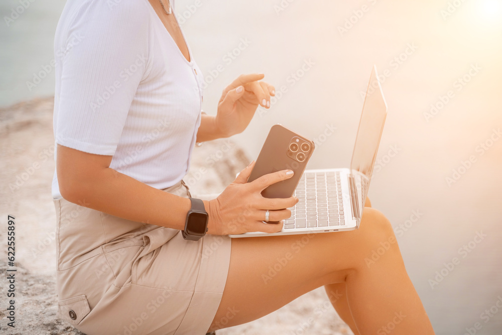 Fototapeta premium Freelance women sea working on the computer. Good looking middle aged woman typing on a laptop keyboard outdoors with a beautiful sea view. The concept of remote work.