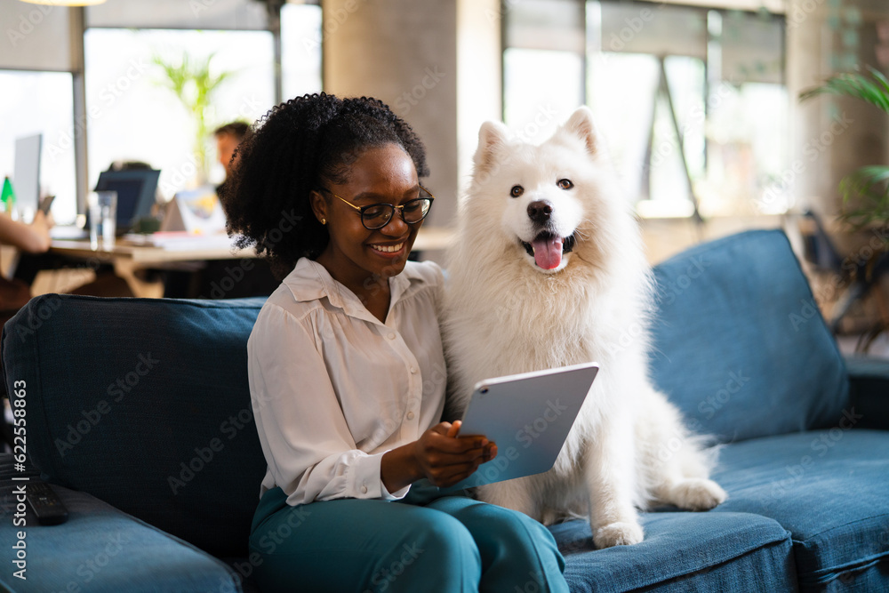 Beautiful African businesswoman sitting on sofa in office enjoying with dog. Young woman having video call. Beautiful African businesswoman sitting on sofa in office enjoying with dog. Young woman having video call.