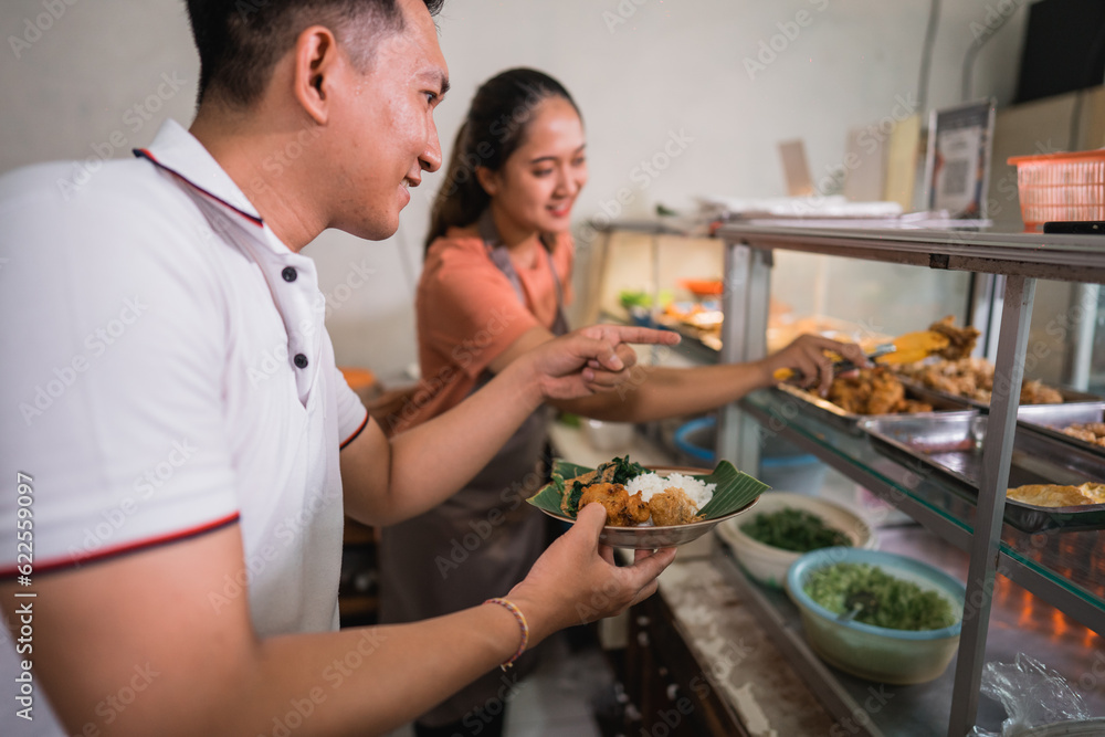 closeup of a handsome man choosing food with pointing finger with a female waitress at a traditional stall