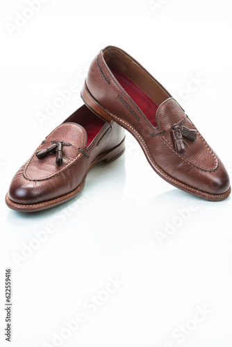 Footwear Concepts. Pair of Traditional Formal Stylish Brown Pebble Grain Tassel Loafer Shoes On White Reflective Surface.