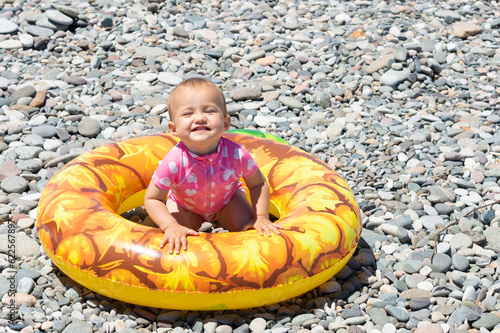 little happy smiling girl with giant rubber swimming ring on the beach by the sea