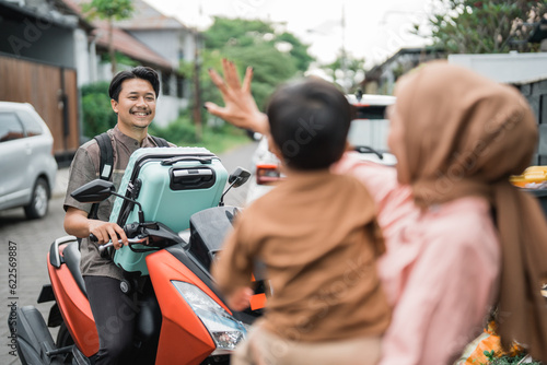 muslim man going by motorcycle scooter leaving his family behind at home. concept of asian family travelling