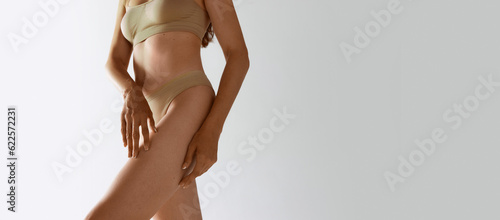 Cropped image of slim, healthy female body, legs over grey studio background. Model posing in underwear. Depilation, epilation. Concept of female beauty, body care, fitness, sport, health, figure, ad