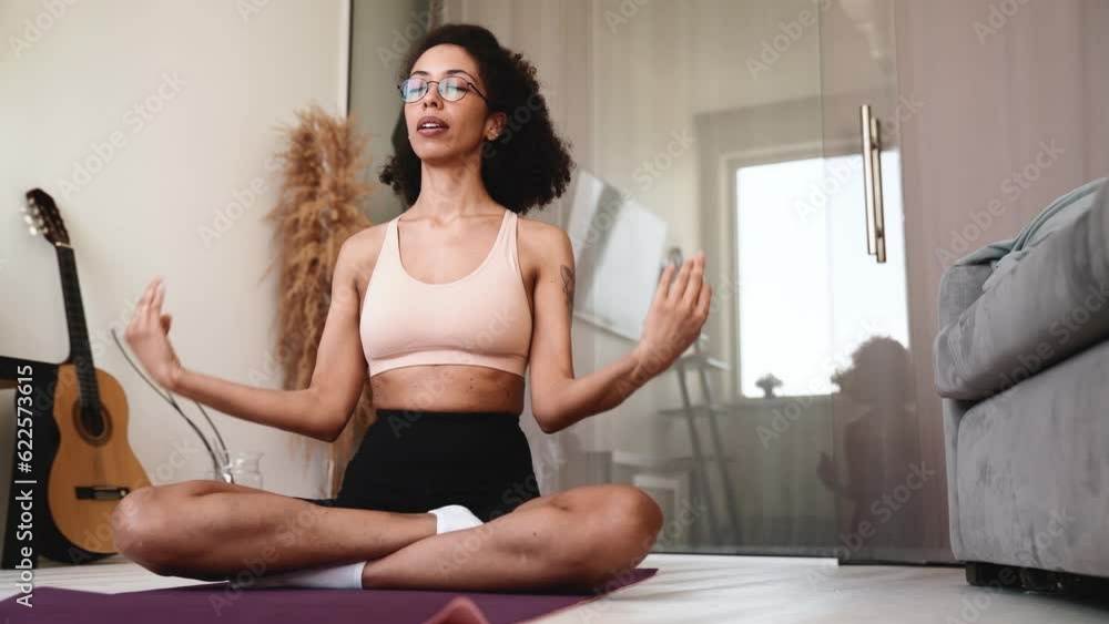Lovely african woman in glasses meditating on yoga mat with closed eyes at home Lovely african woman in glasses meditating on yoga mat with closed eyes at home