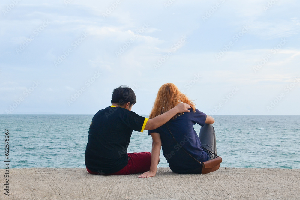 Friend or couple lover siting on mortar. Man put one arm around another is shoulder with women is gold hair. Couple looking at the sea. comforting, sweet couple, travel, Friend Forever concept.