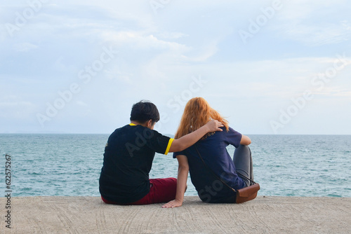 Friend or couple lover siting on mortar. Man put one arm around another is shoulder with women is gold hair. Couple looking at the sea. comforting, sweet couple, travel, Friend Forever concept.