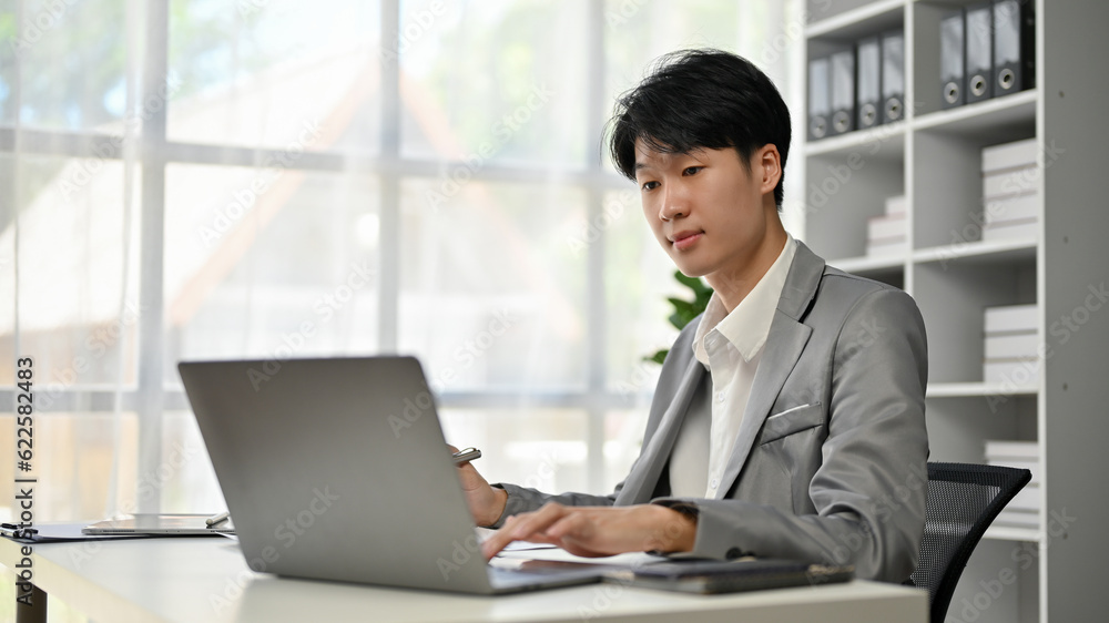 A handsome and smart Asian businessman focuses on his business work on his laptop A handsome and smart Asian businessman focuses on his business work on his laptop