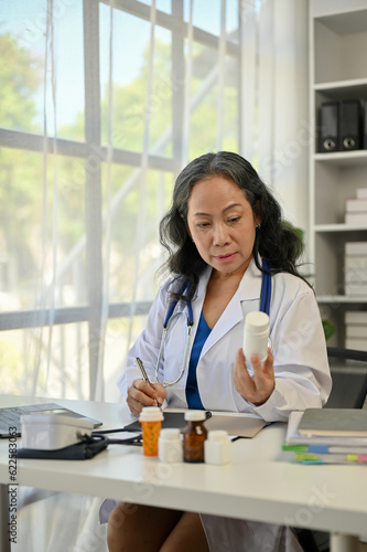 A professional Asian senior female doctor writing medicine prescriptions and working at her desk