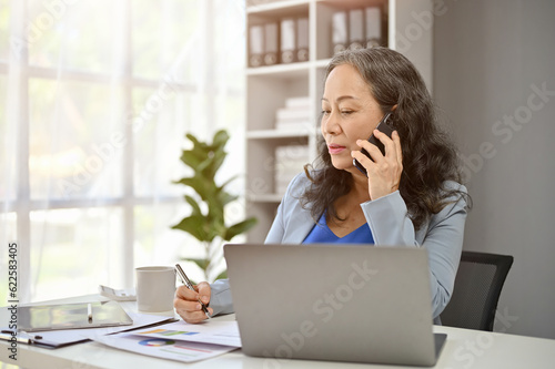 A professional mature Asian female boss is on the phone with a supplier to deal a new contract