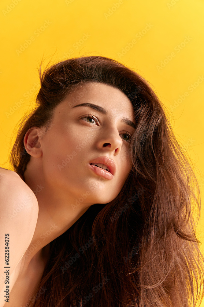 Portrait of young beautiful woman wit brown wavy hair posing against yellow studio background. Self-care. Cosmetology. Concept of female beauty, skin care, cosmetics, spa, health, figure, ad Portrait of young beautiful woman wit brown wavy hair posing against yellow studio background. Self-care. Cosmetology. Concept of female beauty, skin care, cosmetics, spa, health, figure, ad