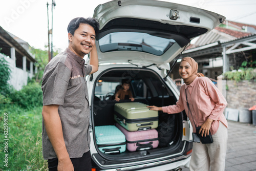 happy asian muslim family with kid sitting in the car trunk with suitcase ready for road trip for eid mubarak holiday