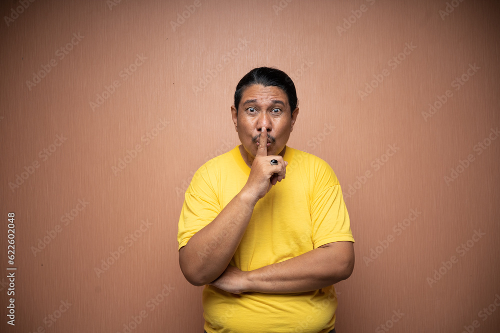 old asian man wearing yellow tshirt with be quiet or shush gesture in plain background isolated old asian man wearing yellow tshirt with be quiet or shush gesture in plain background isolated