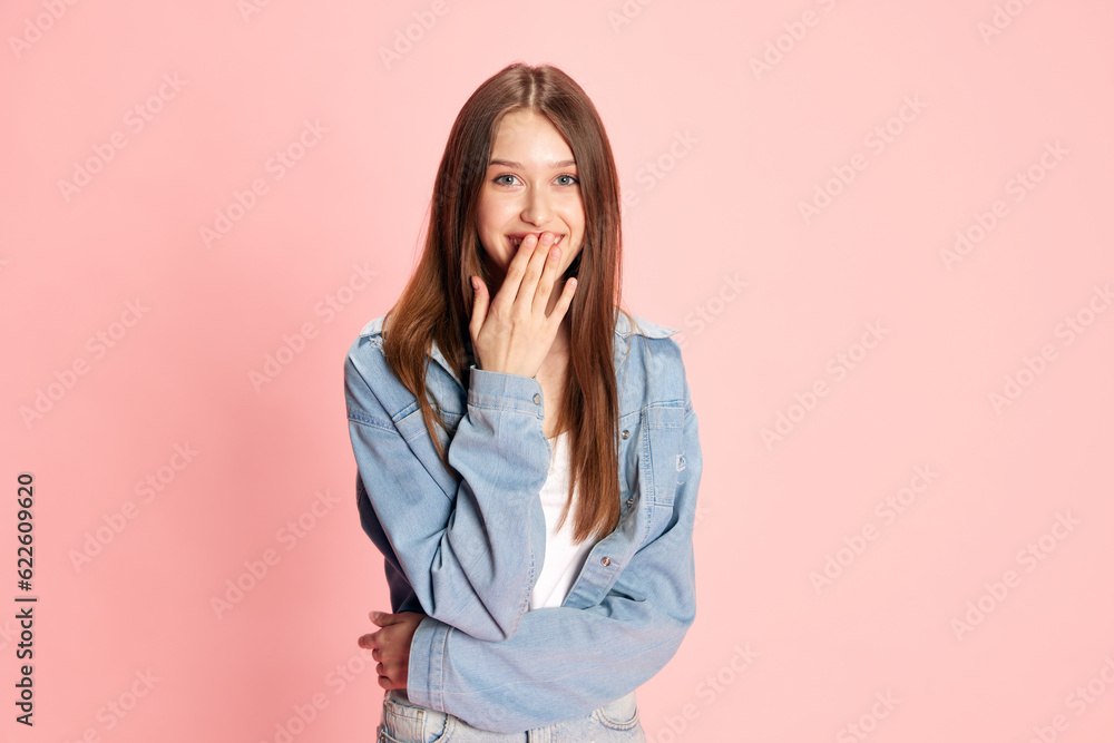 Portrait of young smiling girl covering mouth with hand, feeling surprised against pink studio background. Shocked news. Concept of human emotions, fashion, youth, lifestyle, female beauty, ad Portrait of young smiling girl covering mouth with hand, feeling surprised against pink studio background. Shocked news. Concept of human emotions, fashion, youth, lifestyle, female beauty, ad