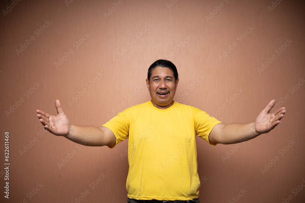 old asian man wearing yellow tshirt with open arm or welcoming gesture in plain background old asian man wearing yellow tshirt with open arm or welcoming gesture in plain background