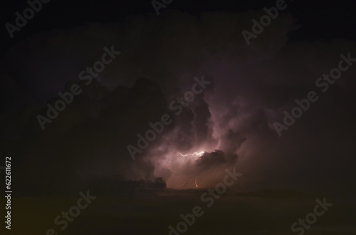 Visione su tempesta nel cielo di Torino, con saetta e fulmine verso il terreno. Contrasto tra ampie nuvole temporalesce scure e luce al centro. Fotografia pittorica.