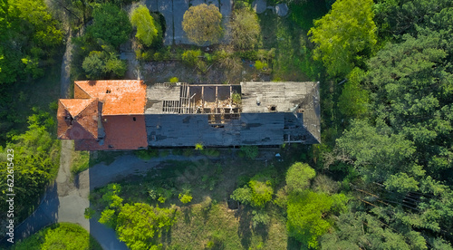 Destroyed abandoned large building in the forest in the mountains. Trees began to grow in the building, nature absorbs the structure. Top view from a drone, in early spring the whole forest is green