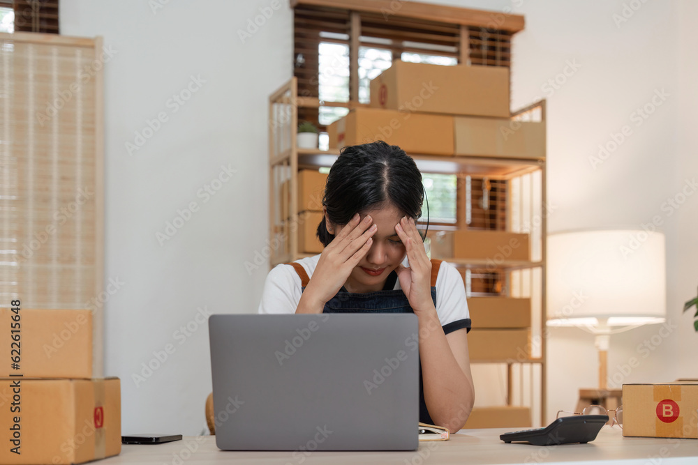 Small online business owner Asian woman wearing apron stressed headache taking Less sales, returned products at home Small online business owner Asian woman wearing apron stressed headache taking Less sales, returned products at home