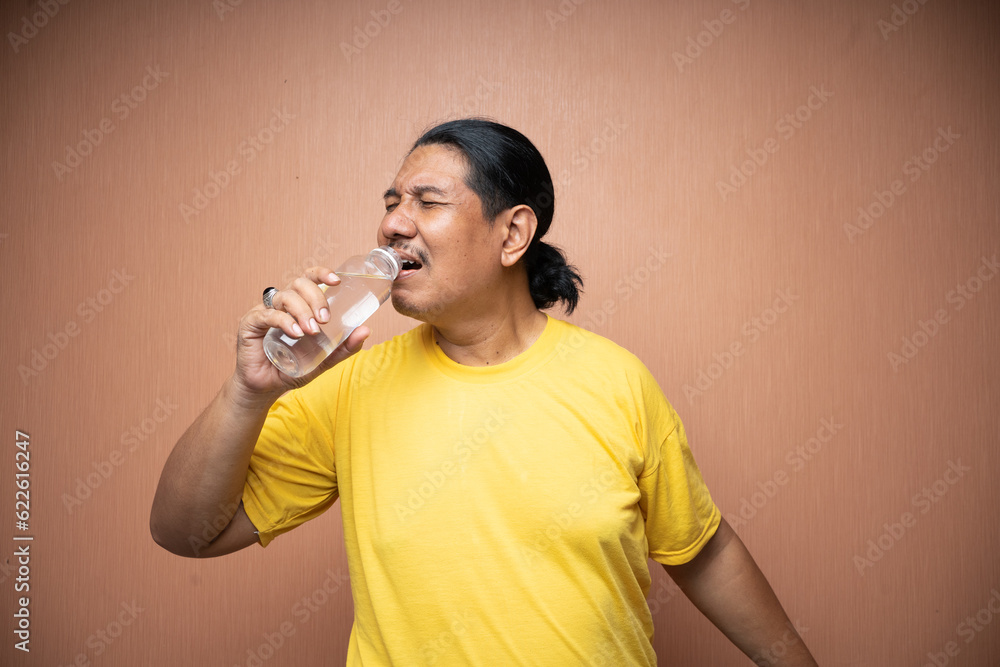 old asian man holding and drinking from unlabelled plastic bottle in plain background isolated old asian man holding and drinking from unlabelled plastic bottle in plain background isolated