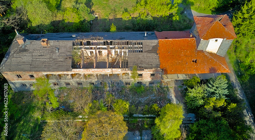Destroyed abandoned large building in the forest in the mountains. Trees began to grow in the building  nature absorbs the structure. Top view from a drone  in early spring the whole forest is green