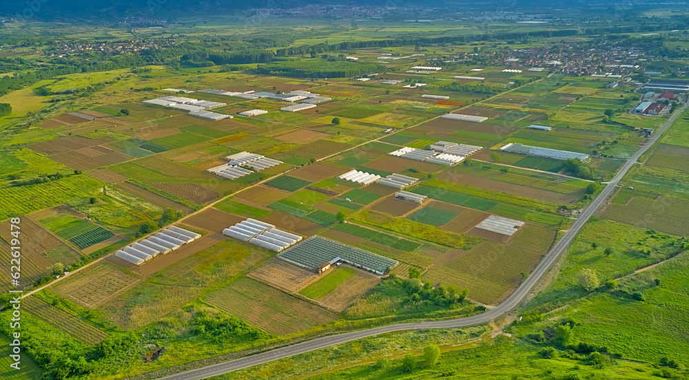 Fototapeta premium Green agricultural fields with various crops and greenhouses to protect plants from bright sunlight and hot weather in a garden plot. Panoramic top view from a drone