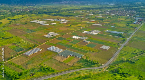 Green agricultural fields with various crops and greenhouses to protect plants from bright sunlight and hot weather in a garden plot. Panoramic top view from a drone