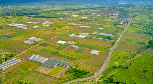 Green agricultural fields with various crops and greenhouses to protect plants from bright sunlight and hot weather in a garden plot. Panoramic top view from a drone
