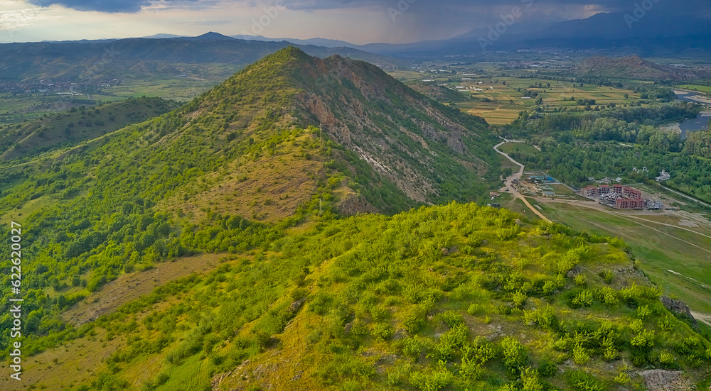 Panoramic drone view of the mountains and the valley with the village at the foot of the mountains in early spring, in front of the approaching thunderclouds. Rupite area (Church of Vanga), Bulgaria