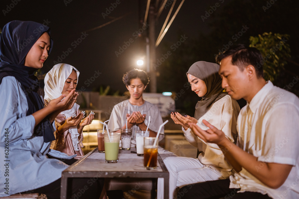 a group of young asian people praying together before breaking fast at outdoor cafe