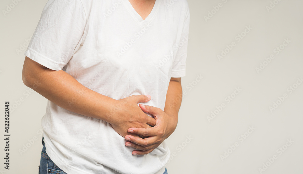 A woman is suffering from stomach ache while standing on a gray background. A woman is suffering from stomach ache while standing on a gray background.