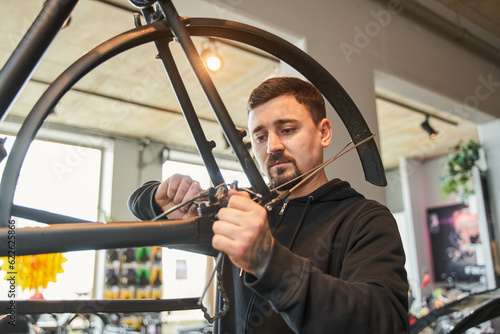 Young caucasian repairman guy installing bike cassette on wheel in modern workshop