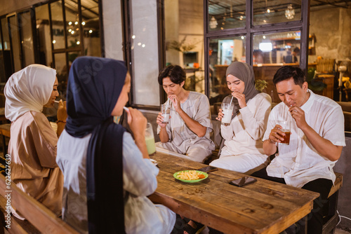 a group of veiled Muslim women and Muslim men drinking through straws from a glass during iftar together