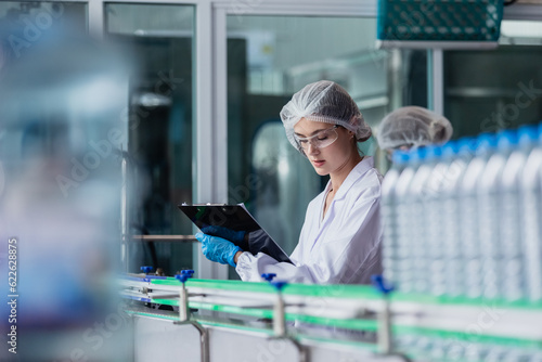 woman factory worker sterile uniform manufacture drink water. Female specialist factory line for processing and checking bottles water. Industrial product manufacturing aqua drink.