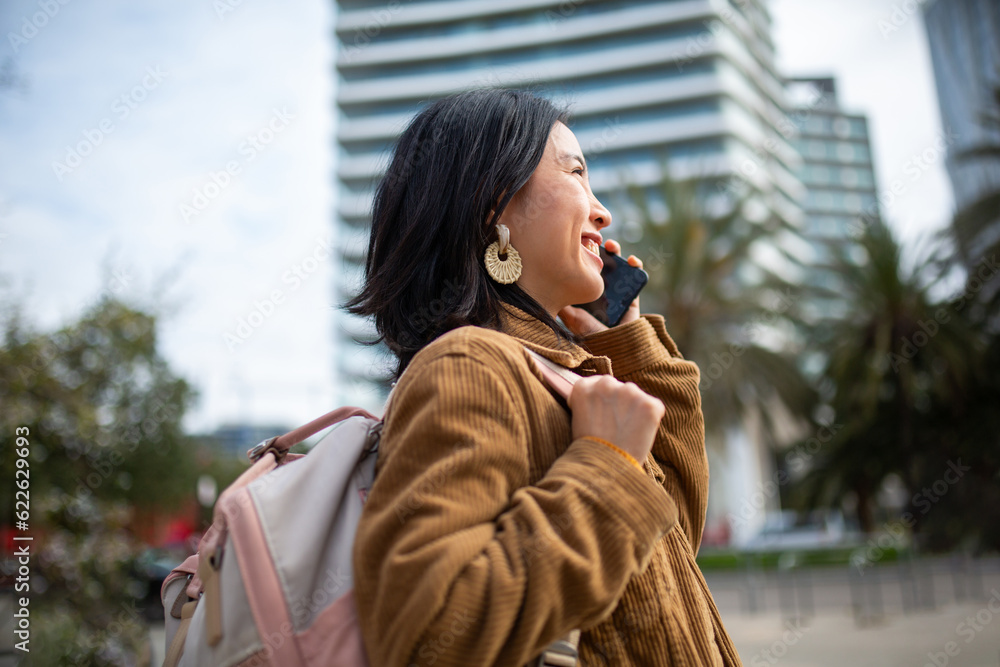 Fototapeta premium Side of young woman walking with bag and mobile phone