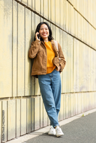Full body smiling young asian woman talking with phone