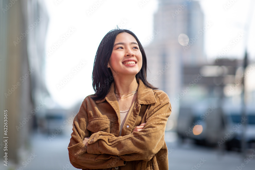 happy young woman standing in city with arms crossed