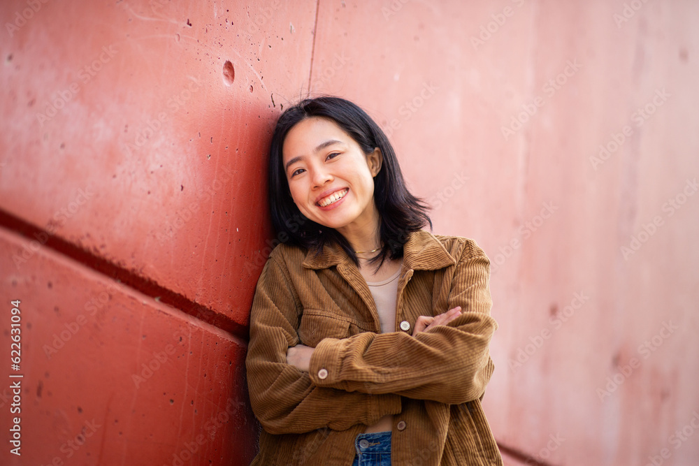 happy young asian woman with arms crossed leaning against wall happy young asian woman with arms crossed leaning against wall