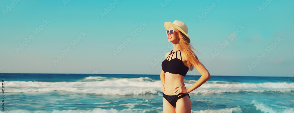 Naklejka premium Summer vacation, beautiful happy smiling woman looking away in bikini swimsuit and straw hat on the beach on sea coast with waves background