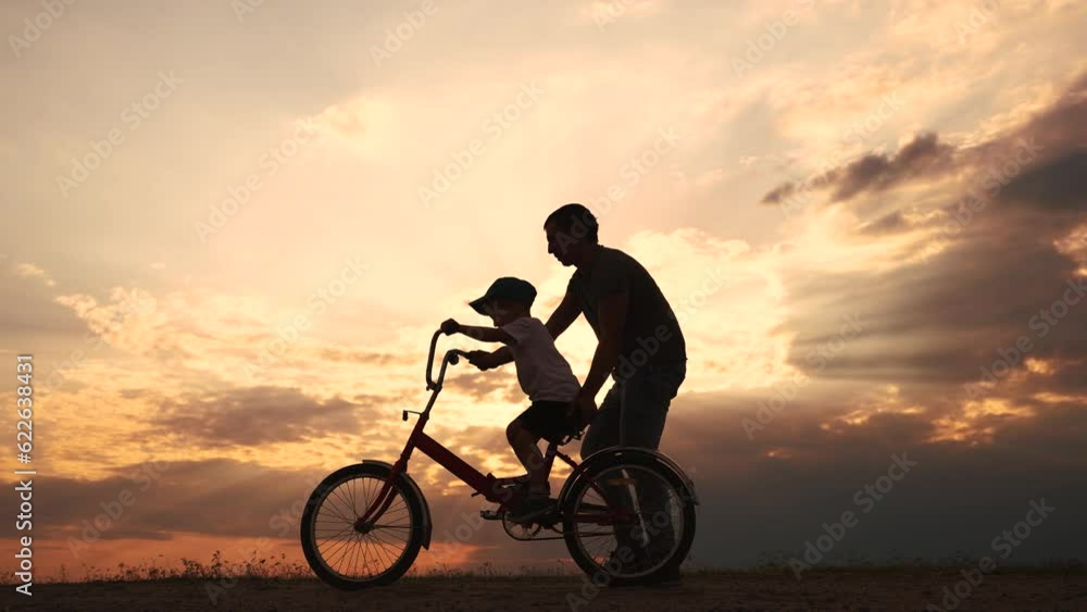 happy family in the park. father teaching son to ride a bike at sunset silhouette in the park. son child learning to ride a bike at sunset father helping son. child playing riding a bike lifestyle happy family in the park. father teaching son to ride a bike at sunset silhouette in the park. son child learning to ride a bike at sunset father helping son. child playing riding a bike lifestyle