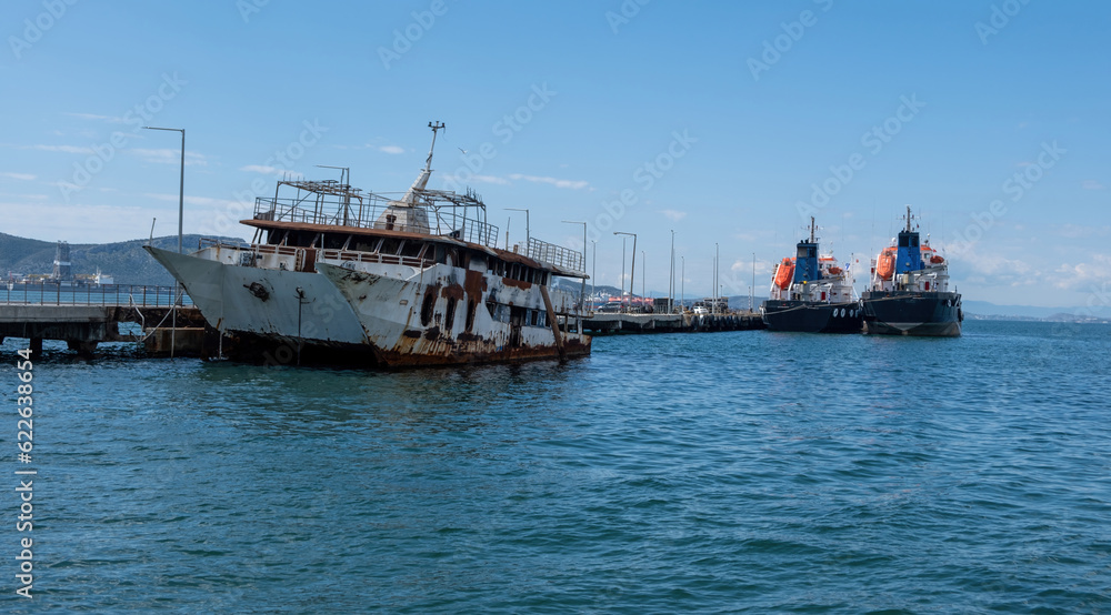Elefsina Attica Greece. Abandoned burned ship moored at port. Tilted rusty shipwreck in calm sea.