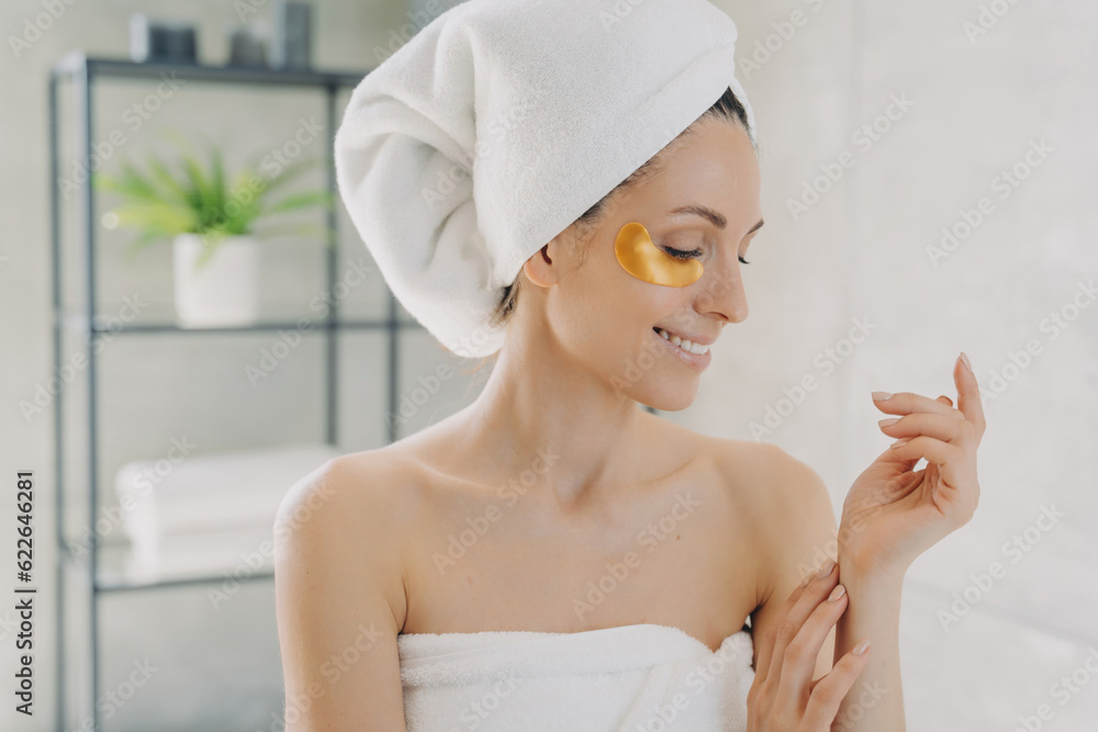 Happy girl uses gold eye patches, cares for silky hands. Attractive European in towel post-spa. Young Hispanic lady does hair and body care at home. Happy girl uses gold eye patches, cares for silky hands. Attractive European in towel post-spa. Young Hispanic lady does hair and body care at home.