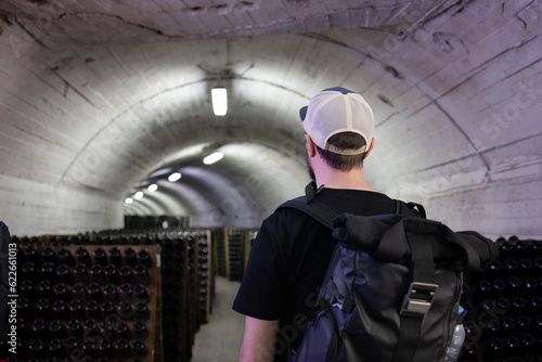 Billede på lærred Back view a tourist with a backpack stands at the production of champagne