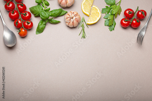 Composition with branch of fresh cherry tomatoes, herbs, garlic cloves, lemon wedges, kitchen spoon and fork on minimalistic gray clean background, overhead shot with copy space