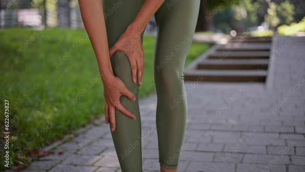 Sport traumas concept. Unrecognizable woman jogger running in park and feeling acute pain in knee, massaging painful leg during morning run outdoor, close up, slow motion. Leg muscle cramp calf sport. Sport traumas concept. Unrecognizable woman jogger running in park and feeling acute pain in knee, massaging painful leg during morning run outdoor, close up, slow motion. Leg muscle cramp calf sport.