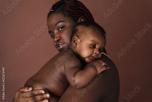 Beautiful african mother with her sleeping baby holding and hugging him over isolated brown background