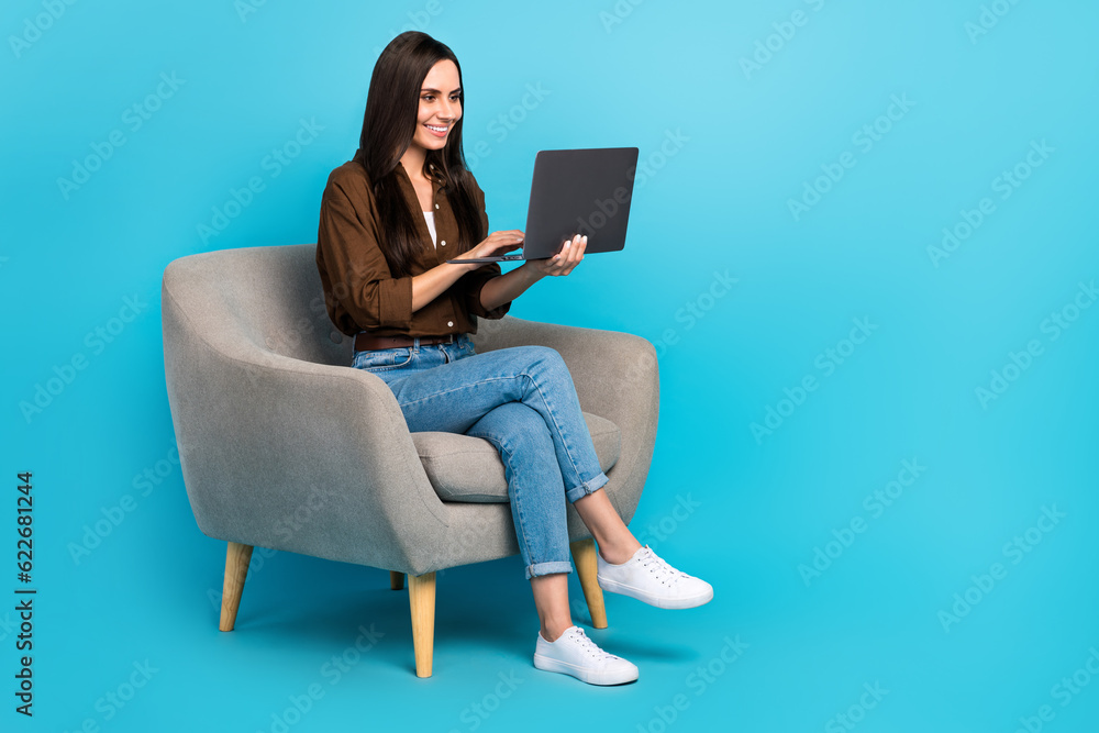 Full body photo of optimistic business meeting worker young woman freelancer using netbook it armchair isolated on blue color background Full body photo of optimistic business meeting worker young woman freelancer using netbook it armchair isolated on blue color background