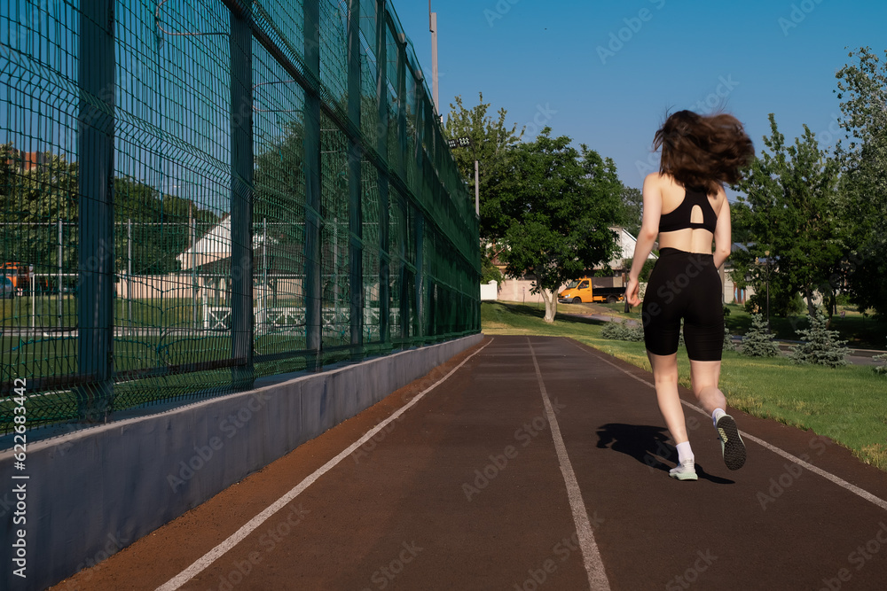 a woman in sportswear works out at a sports stadium. Fit woman jogging outdoors. Warm-up in the morning. Healthy and active lifestyle concept, fitness silhouette, sunrise, jogging wellness workout