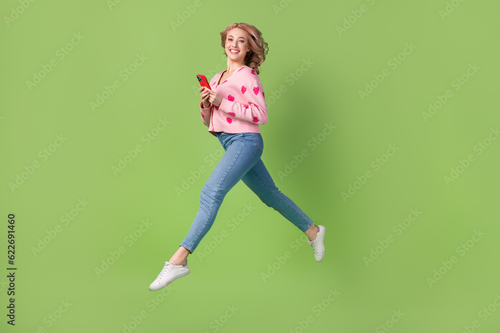 Full length profile portrait of charming cheerful person jumping run hold smart phone isolated on green color background Full length profile portrait of charming cheerful person jumping run hold smart phone isolated on green color background