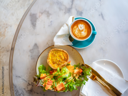 A delectable quiche paired with a steamy cup of coffee, the ideal breakfast duo, invitingly rests on a cool marble surface, adding to the allure of morning indulgence photo