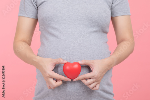 Close up finger of Pregnant woman holding on belly making shaping a heart for love and happiness on pink,Pregnancy of young woman enjoy with future life relax with love,Motherhood and Pregnant Concept