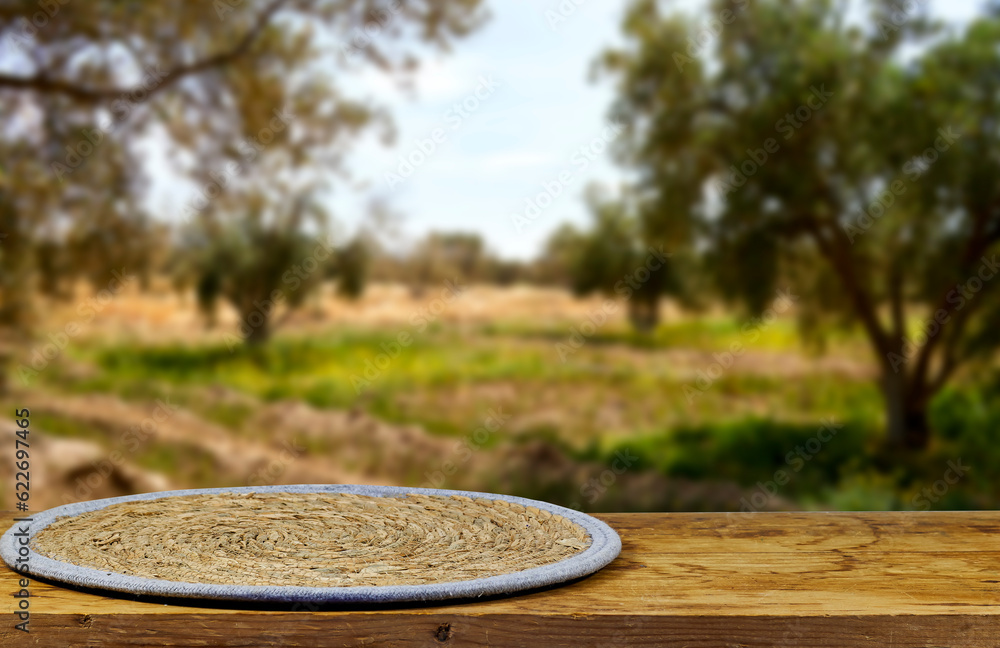 Detail view of  round trivet made of wicker on wooden board near blur olives field